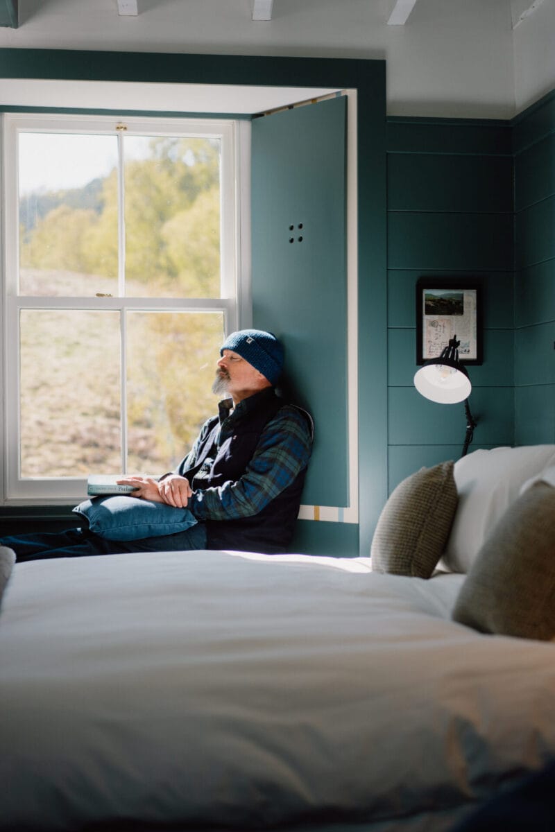 Guest relaxing on the bed in the teal bedroom at Cairn Valley Cottage, Rothiemurchus, Aviemore