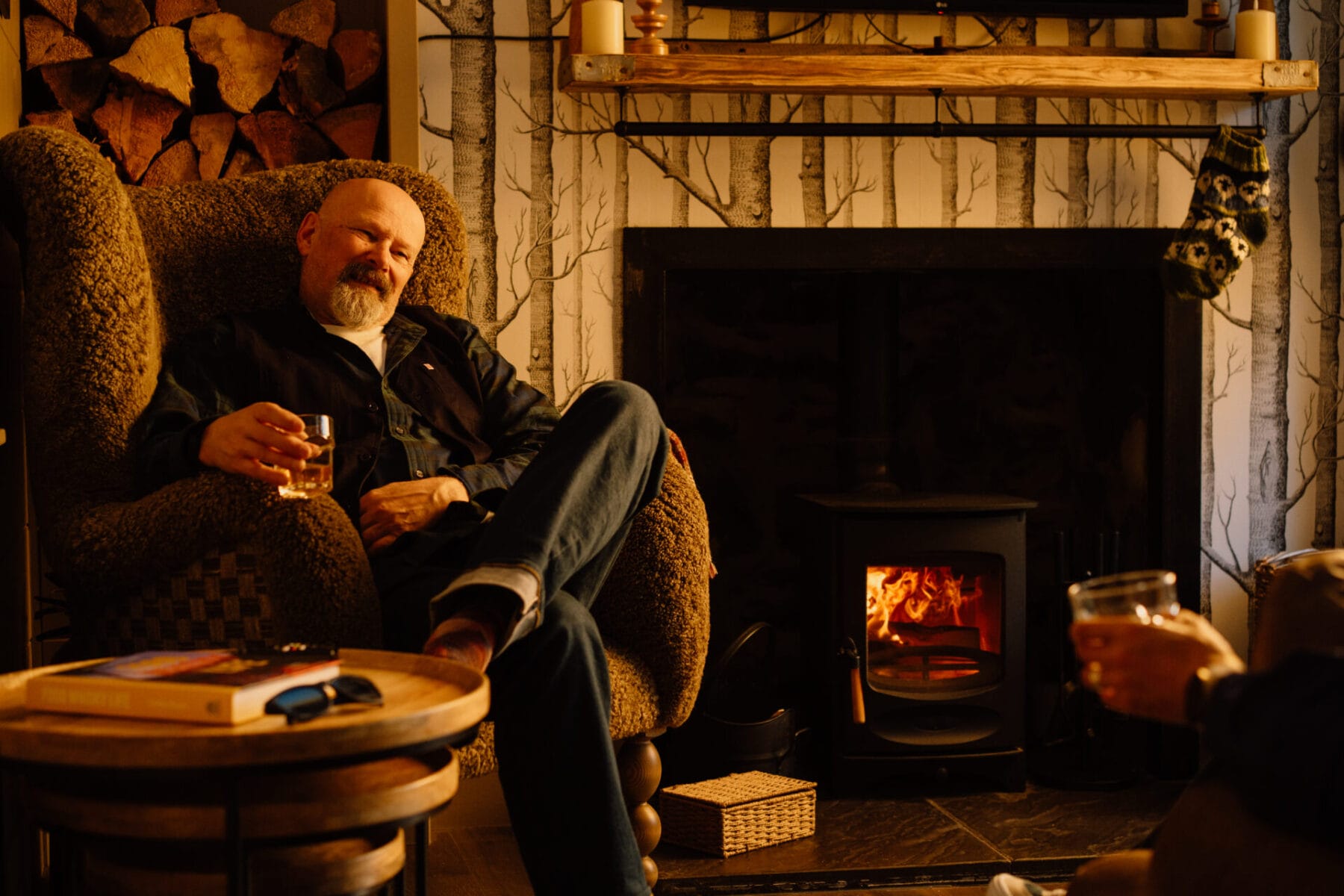 Guest relaxing by the wood-burning stove at Cairn Valley Cottage, Rothiemurchus, Aviemore