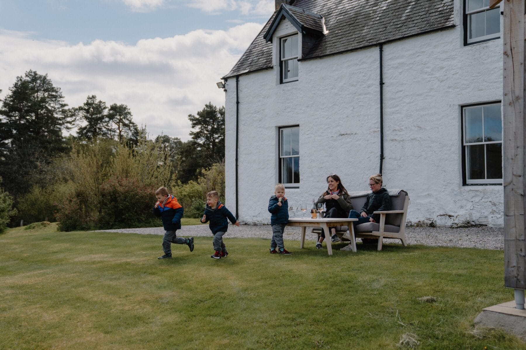 White farmhouse with the family in the garden at Achnahatnich House, Rothiemurchus, Aviemore